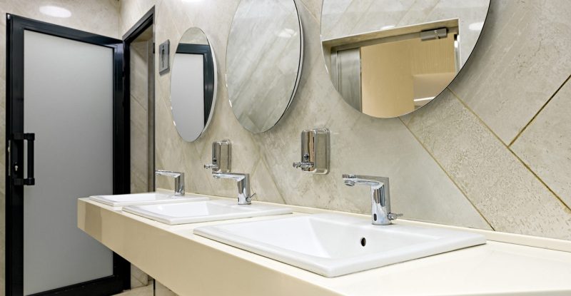 A bathroom vanity area, three sinks on a countertop, and three circular mirrors against a tiled wall