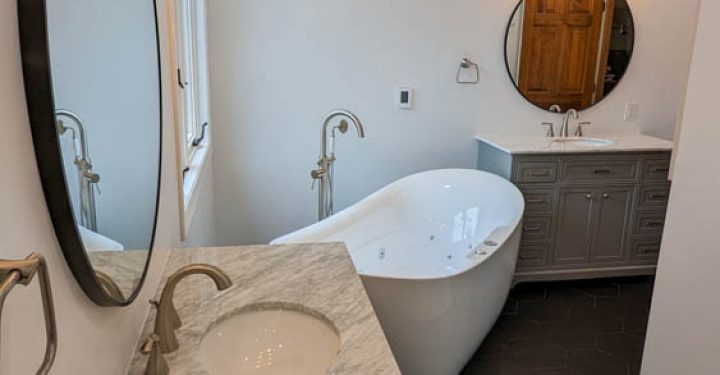 Freestanding Tub in a bathroom with free standing faucet, a casement type window, warm light fixtures, and vanity cabinets for bathroom storage