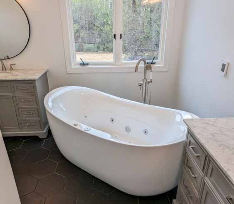 Freestanding Tub in a bathroom with free standing faucet, a casement type window, and vanity cabinets for bathroom storage