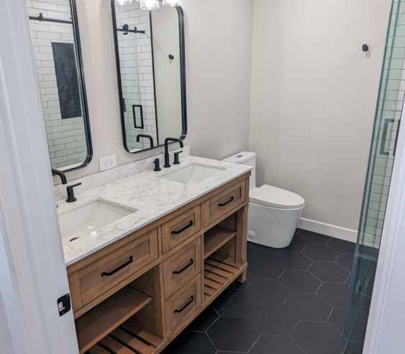 Bathroom; view from the outside, a vanity cabinet with two sink and two mirrors with wall mounted pendant lights, large dark blue hexagonal flooring tiles
